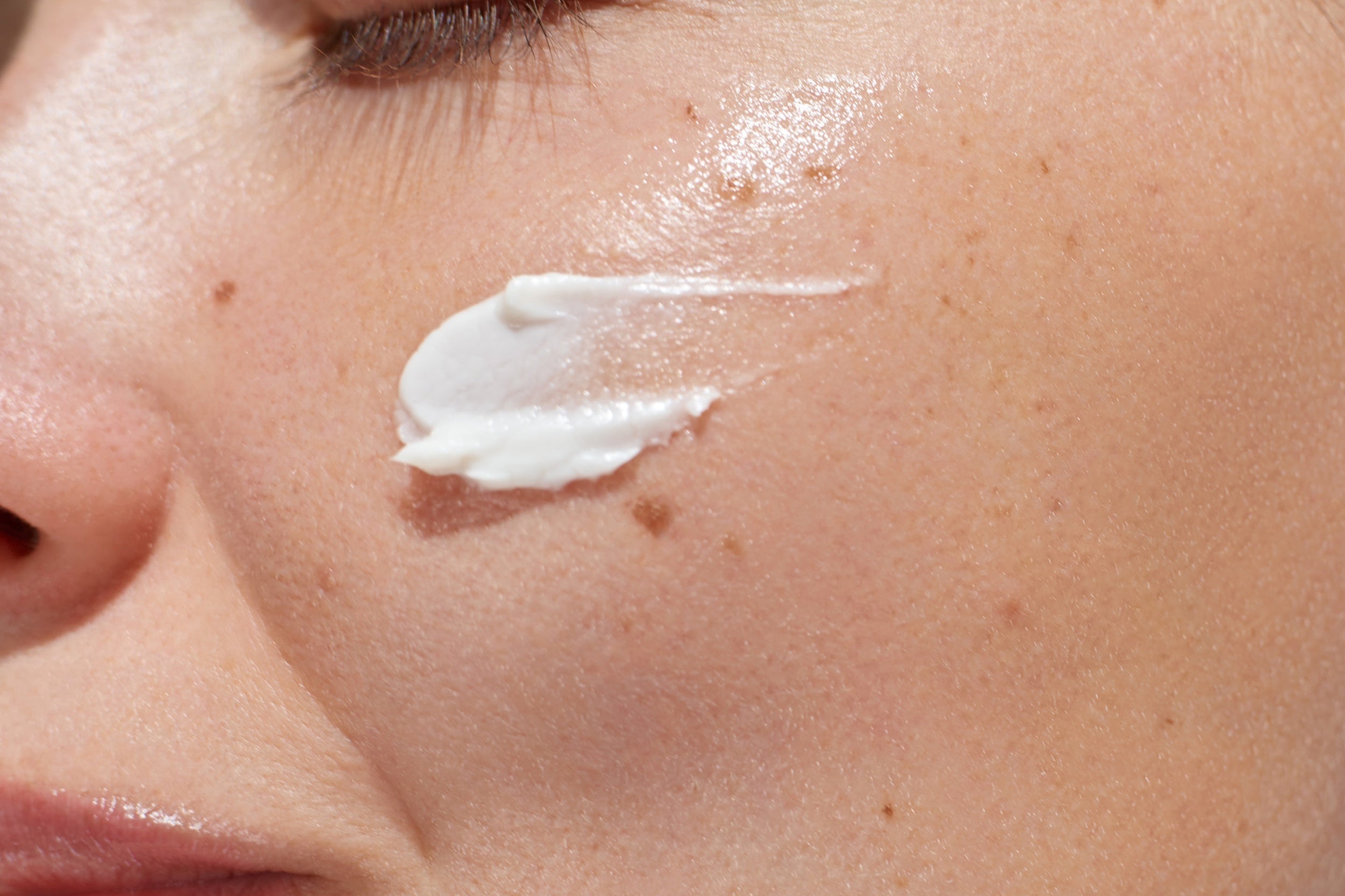 Close up portrait of a woman with a healthy skin applying a moisturizing skincare product.