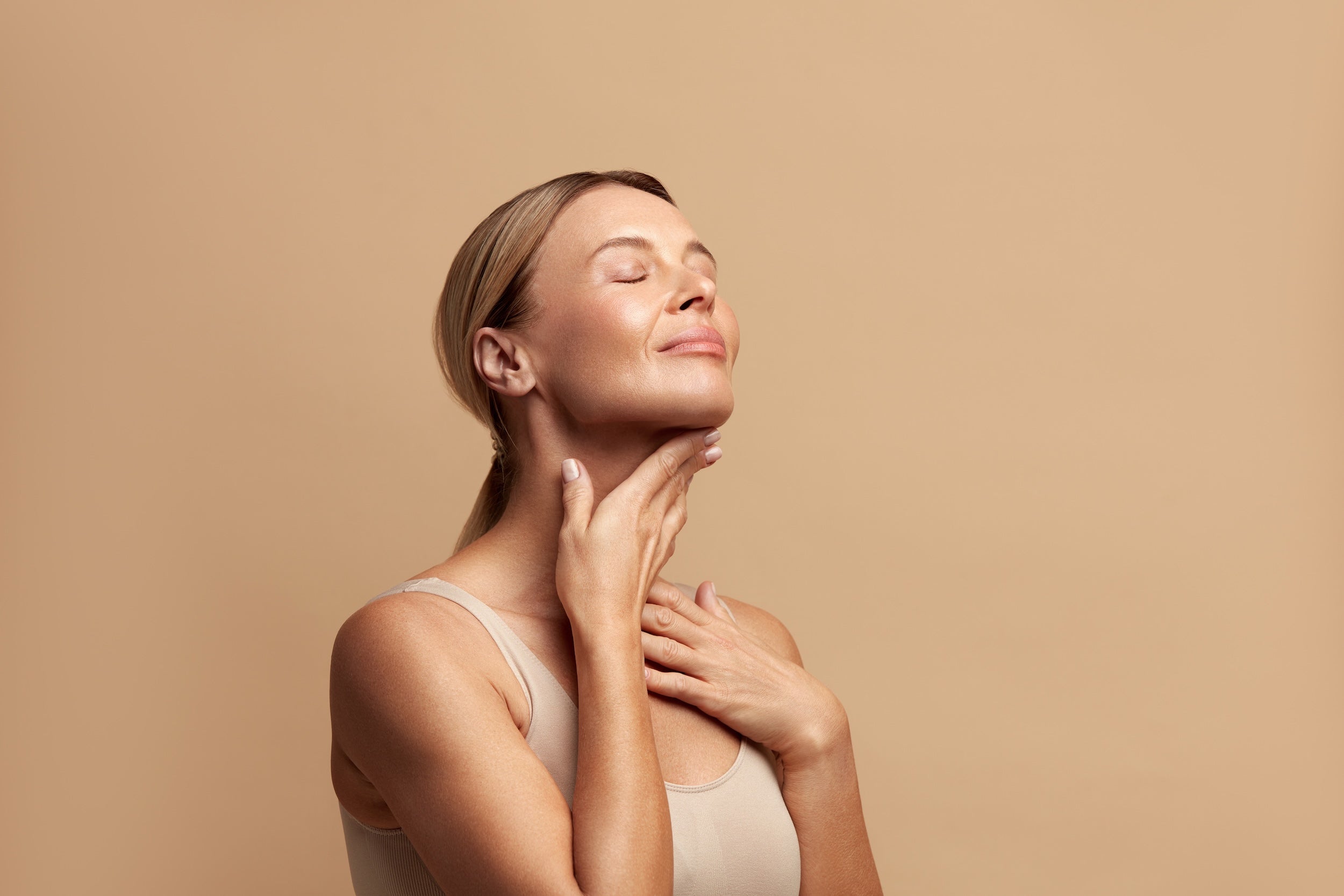 Waist up Portrait of a Woman Touching her Skin and Smiling with Closed Eyes.